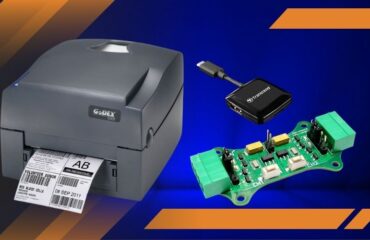 GoDEX label printer printing a tag, with a USB adapter nearby and a green circuit board on a blue background, showcasing electronics.