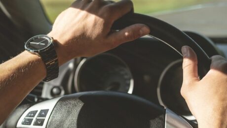 Vybir spidometra pid konkretnu model vantazhivky tablytsya sumisnosti 2026 roku Driver's hands on a car steering wheel, wearing a metal wristwatch on the left wrist.