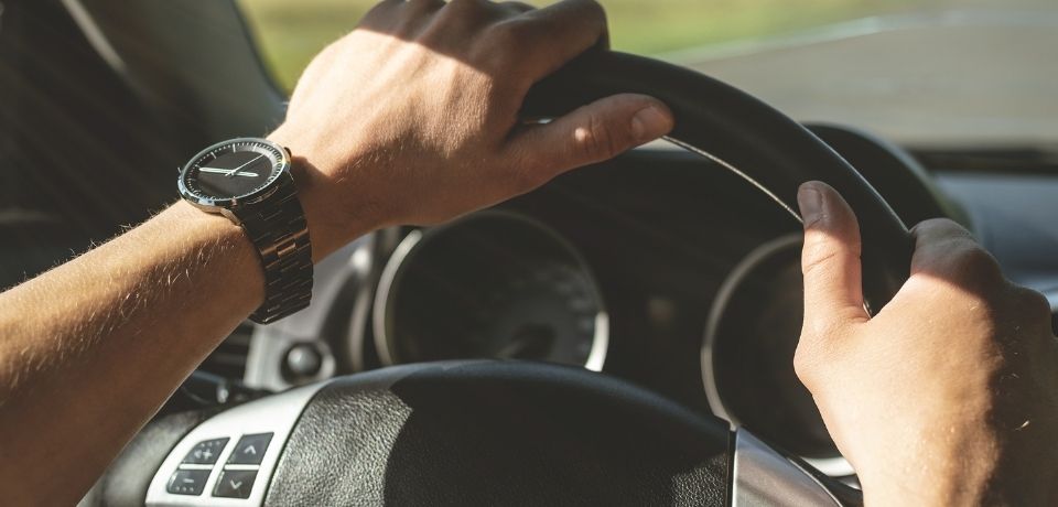 Vybir spidometra pid konkretnu model vantazhivky tablytsya sumisnosti 2026 roku Driver's hands on a car steering wheel, wearing a metal wristwatch on the left wrist.