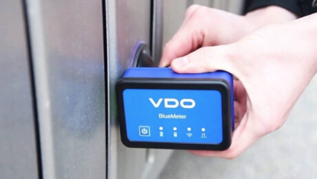 BlueMeter i bezdrotovi fotoelementy tochnist kalibruvannya bez zayvykh kabeliv Hand holding a blue VDO BlueMeter device against a metal door lock.