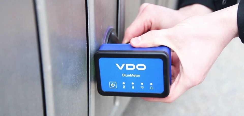 BlueMeter i bezdrotovi fotoelementy tochnist kalibruvannya bez zayvykh kabeliv Hand holding a blue VDO BlueMeter device against a metal door lock.
