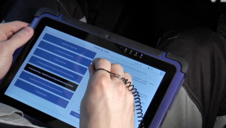 WorkshopTab 2 vid VDO novyy standart u kalibruvanni takhohrafiv Person using a stylus to interact with a blue-screen tablet in a rugged purple case, selecting menu items.