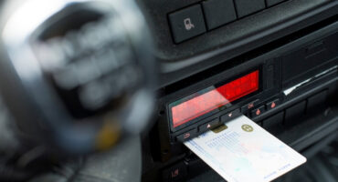 Close-up of a credit card being inserted into a car's dashboard payment terminal with a red display in view.